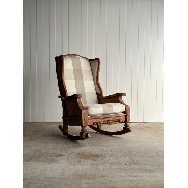 Vintage studio craft rocking chair in solid oak with a tall wingback frame, sculpted arms, and curved rocker base. Carved...
