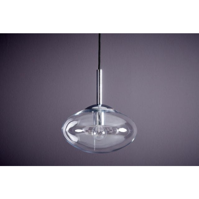 Hand-blown, lens-shaped glass shade encases the light source, producing a soft, atmospheric glow while creating striking...