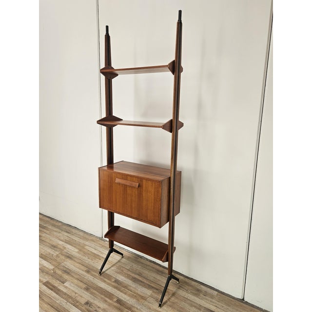 1960s teak veneered bookcase with an iron frame and uprights and adjustable brass feet. The piece features several holes...