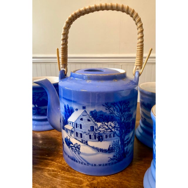 This Currier & Ives Tea Set, comprising a matching teapot with a distinctive wicker handle and four golden trimmed mugs,...