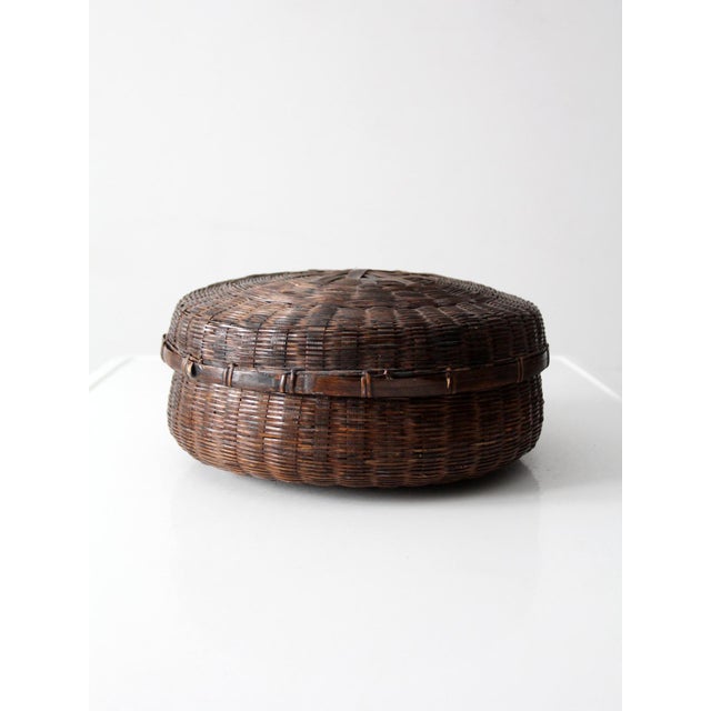 This antique Chinese lidded bamboo basket features a low, rounded form with tightly woven construction and a richly...