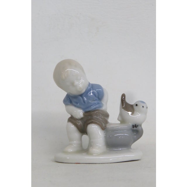 This charming Porcelain Figurine is made of porcelain. This adorable piece features a young boy sitting at a pot with a...