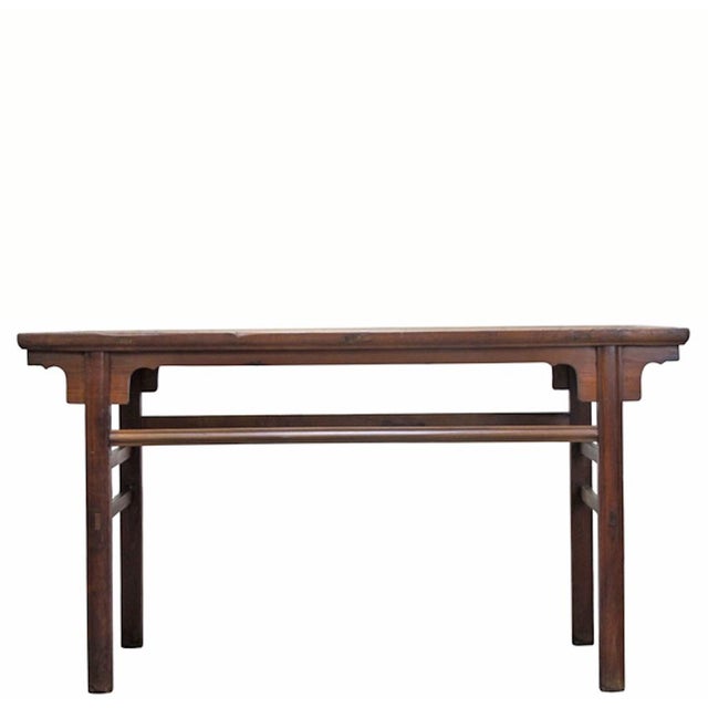 This long, slender console table is crafted from solid elm wood, featuring a rectangular top with a visible natural grain....