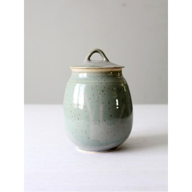 This vintage handmade pottery jar features a serene pale green glaze, delicately speckled with brown and accented with...