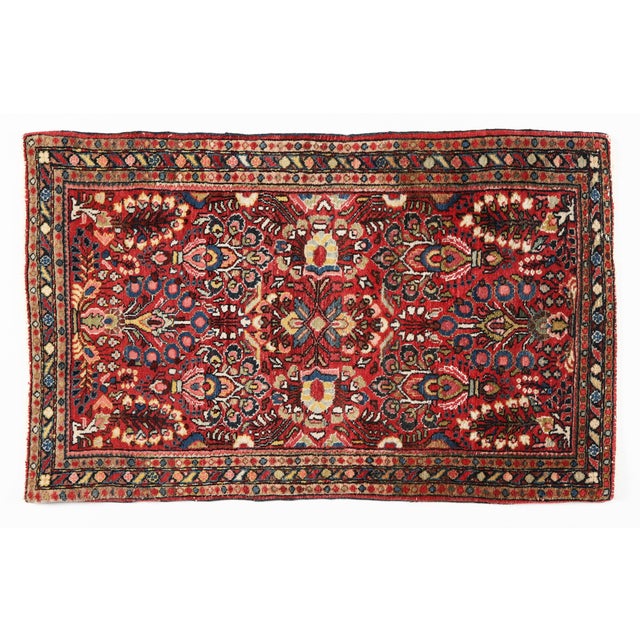 This charming antique Persian Sarouk rug features a vibrant deep red field adorned with intricate floral motifs, lush...