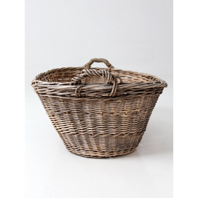 This antique wicker basket features a generous oval form, wrapped handles, and a dark wood base that gives the piece a...