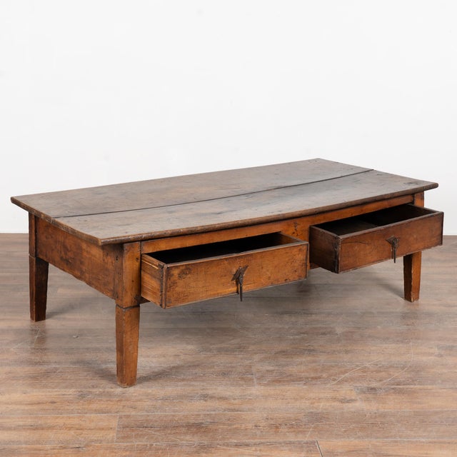 French oak coffee table featuring two drawers fitted with iron hanging pulls. The tabletop is formed from two wide antique...