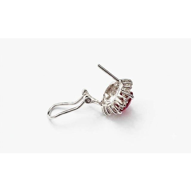 Stunning 18K white gold earrings featuring natural oval rubies surrounded by a sparkling halo of round brilliant and...
