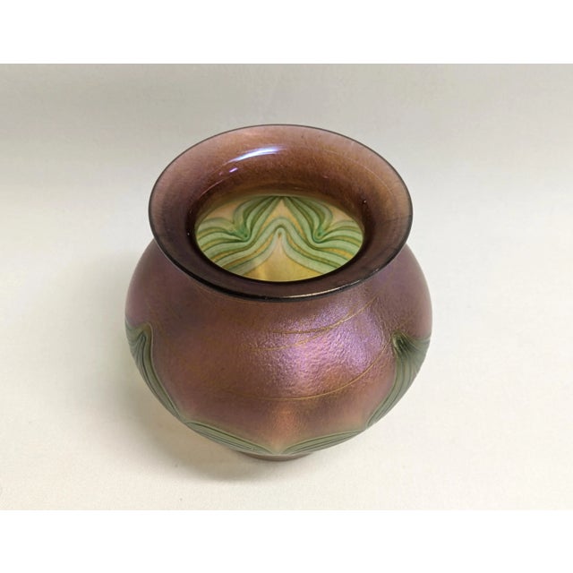 A Czech Republic Bohemian art glass vase in hues of purple, green and gold. The iridescent rose bowl is hand blown and...