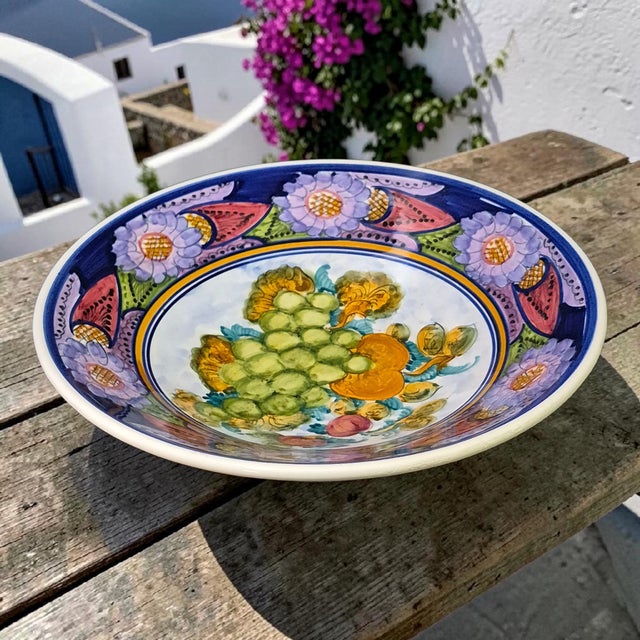This vintage ceramic platter from Greece features hand-painted floral and fruit motifs in vibrant colors. Made by AD in...