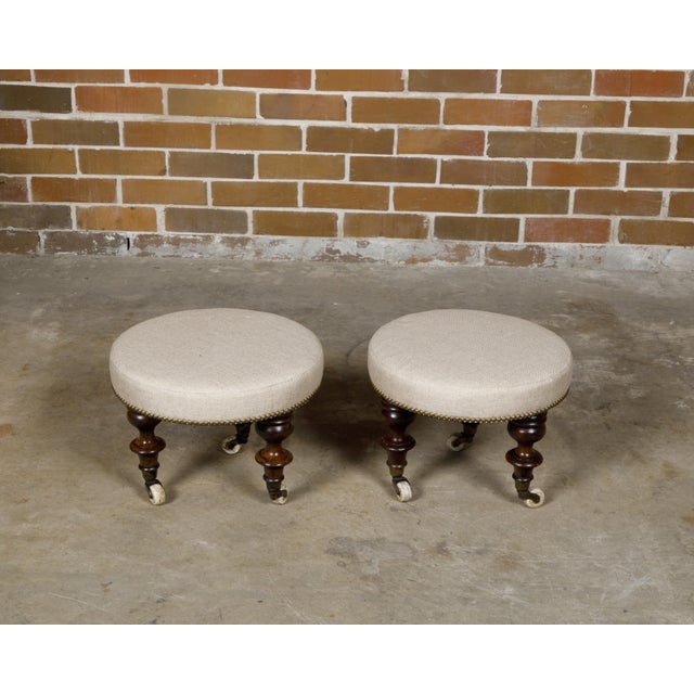 A pair of English mahogany stools from the 19th century with turned legs resting on casters and upholstered seats. This...