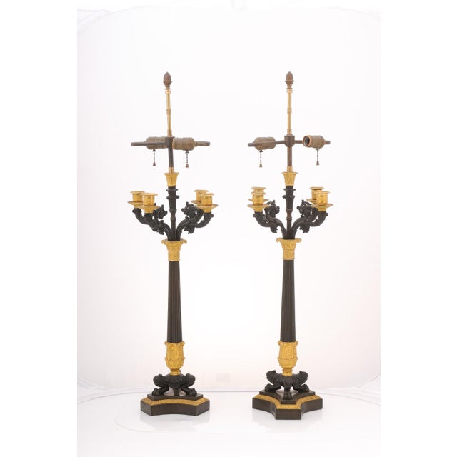 An imposing pair of patinated bronze and gilt French Empire table lamps from the early 20th century. Each lamp features a...