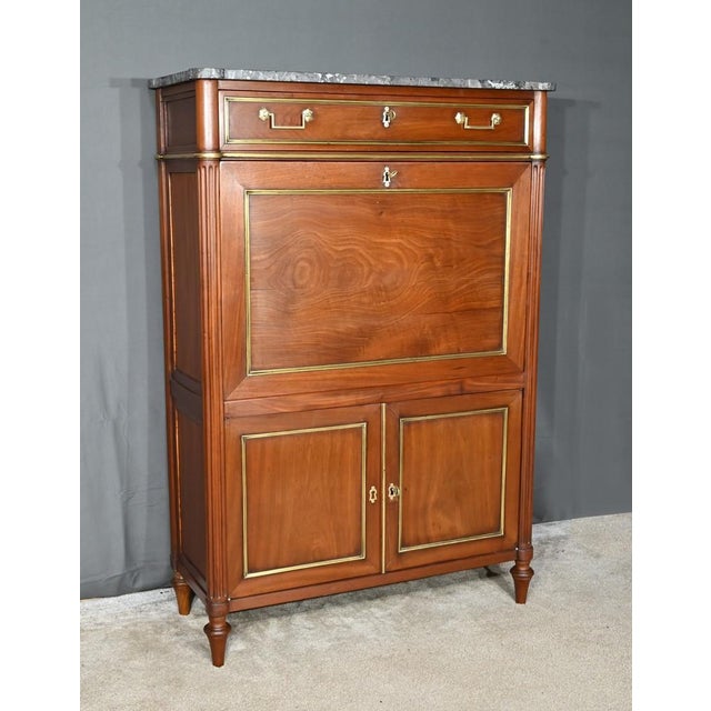 This mahogany secretary opens at the waist with a knockout drawer, highlighted with brass ogee strips, fitted with an...