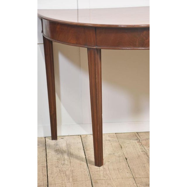 A fine pair of antique mahogany demilune (half-moon) console tables, dating from the 19th century. Each table features a...