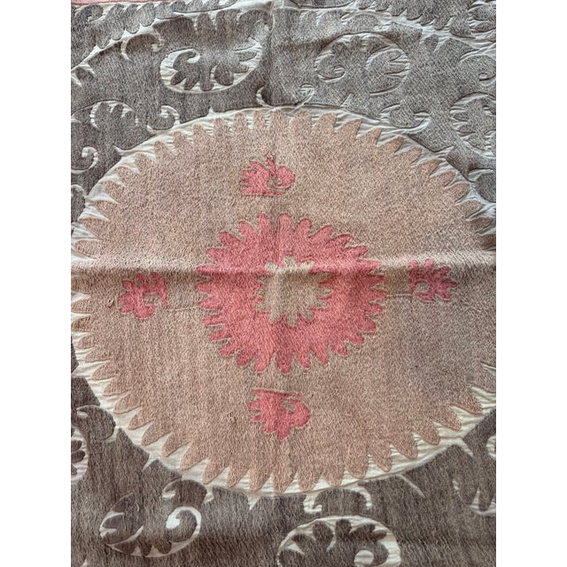 Hand-embroidered Suzani panel from Uzbekistan — a blush pink centre medallion surrounded by taupe leaf scrolls and a rose...