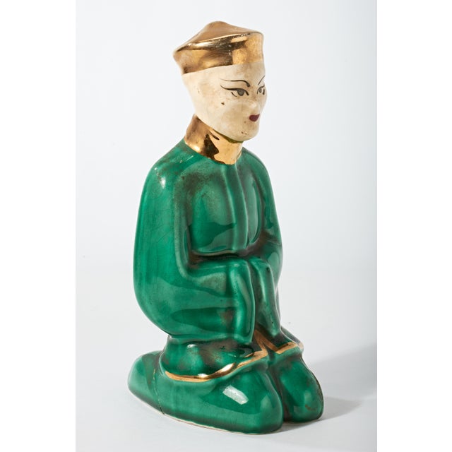 Traditionally clothed Chinese man in simple traditional green clothing with gold accents and headwear. Figure is in...