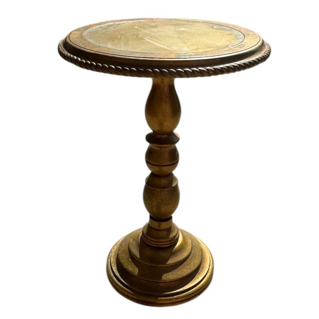 A beautiful round side table with a bright, gold leaf finish with patina. The table has a pedestal base with rope detail...