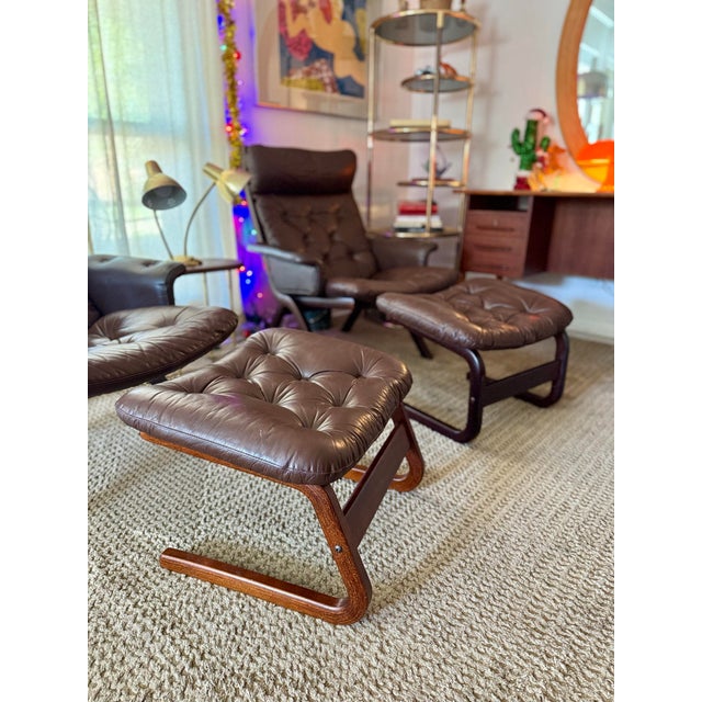 A beautiful vintage Danish Norwegian Ekornes “Uno” lounge chair with stool in a brown leather, circa 1970s. One stool is...