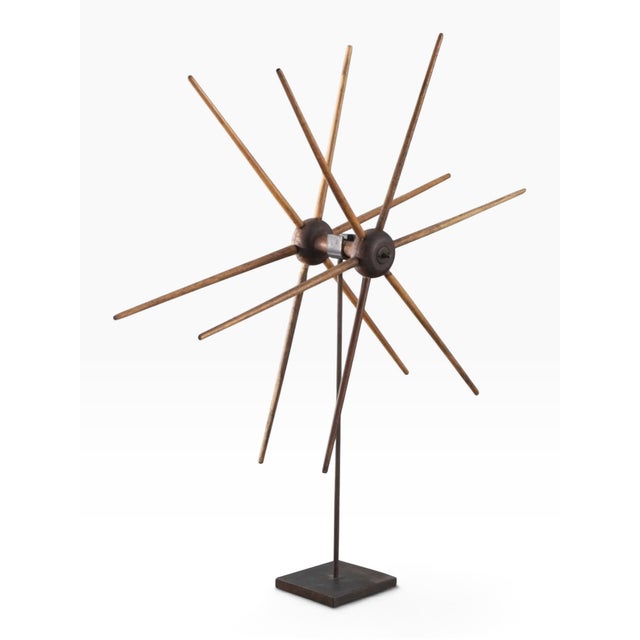 A primitive American spinning wheel made of wood with long spindles, displayed on a custom metal stand. Early 19th century.