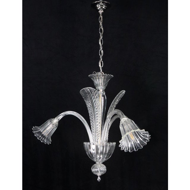 This three-arm Murano style glass chandelier is crafted from hand-blown clear glass with a coordinated ribbed texture. The...