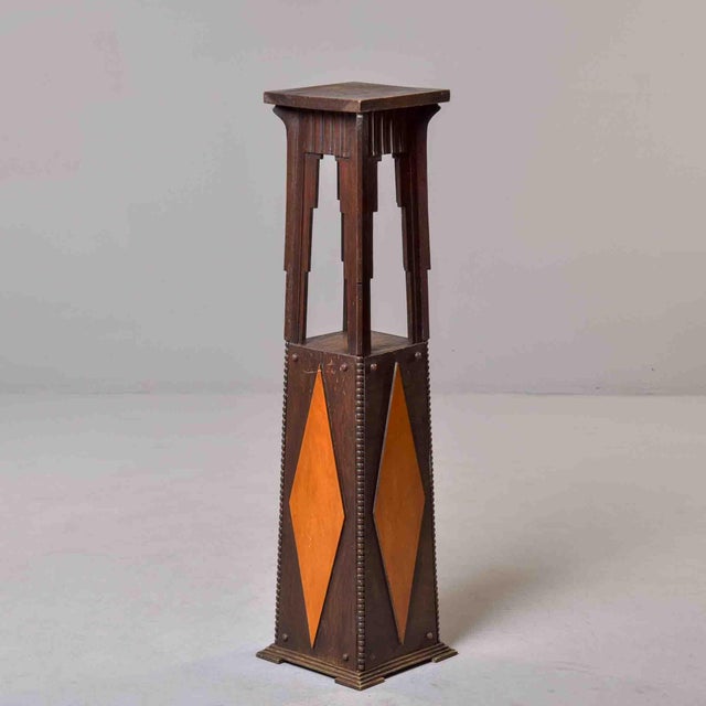 Tall oak pedestal featuring vibrant contrasting diamond inlays in light amber wood. The tapered lower section displays a...
