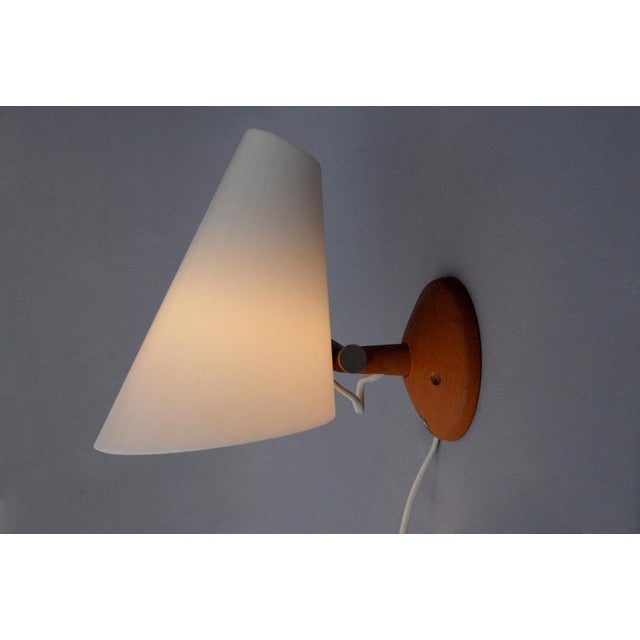 Wall lamp made of a teak stem and wall plate with an white acrylic conical shade. Designed in 1964 by Uno & Östen...
