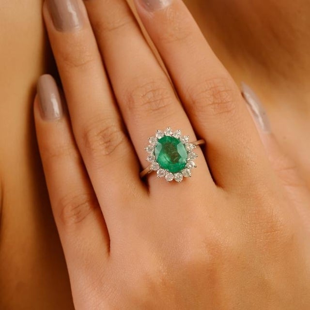 This elegant ring features a 2.26-carat oval-cut Zambian emerald, surrounded by a halo of brilliant round-cut diamonds...