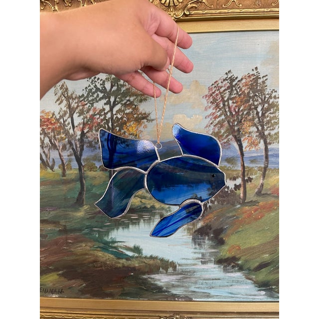 A hand-crafted stained glass fish sun catcher, designed with richly hued cobalt blue glass accented by swirled tonal...