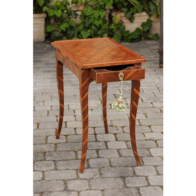An Italian walnut side table from the early 19th century, with marquetry top, lateral drawer and inlaid legs. Born in...