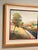 original framed landscape painting by artist R. A. Brandes depicting a serene path or creek alongside trees in soft,...