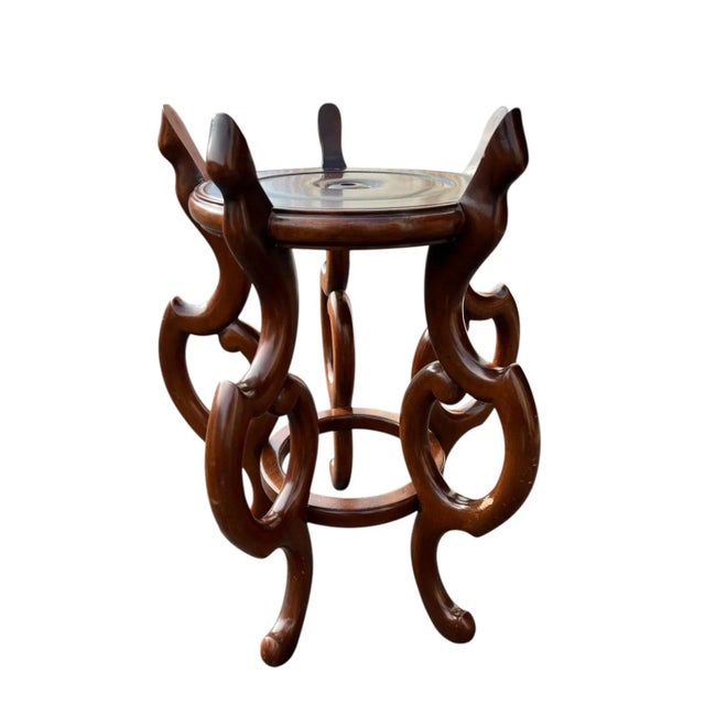 Unique wooden plant stand with a beautiful sculptural base featuring interlocking looped legs and a round top. The rich...