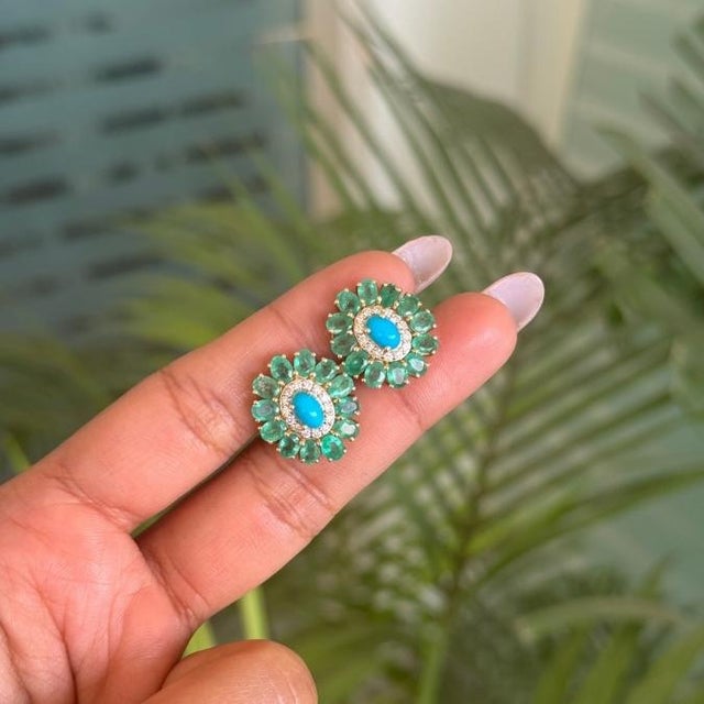 These striking flower stud earrings feature 2 vibrant turquoise center framed by a lush halo of round emeralds totaling...