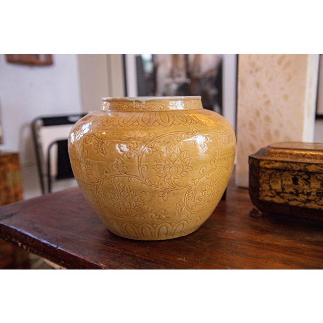 A rounded ceramic pot or vessel finished in a warm mustard glaze, decorated throughout with finely incised floral and...