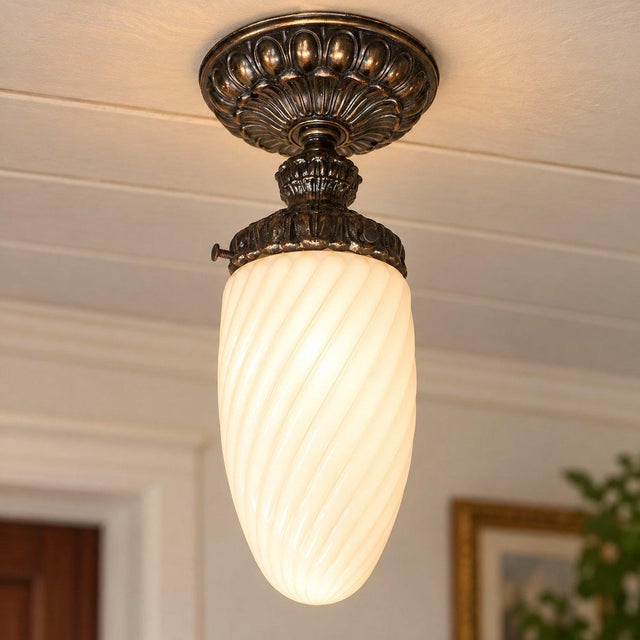 Art Deco-style milk glass flush mount ceiling light with a swirling white glass globe and ornate vintage metal fixture....