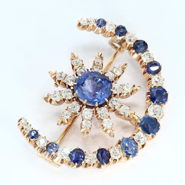 This late Victorian-style brooch features a central blue sapphire surrounded by a radiant array of white diamonds. The...