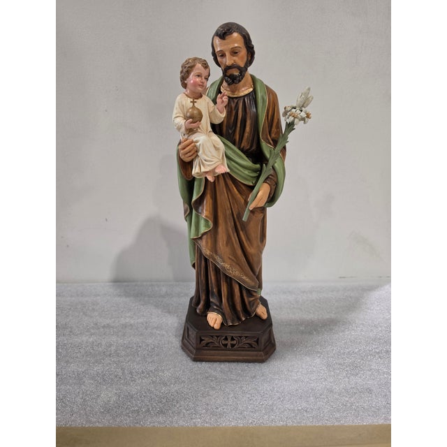 This religious figurine represents Saint Joseph holding the Child Jesus, sculpted with traditional devotional proportions...