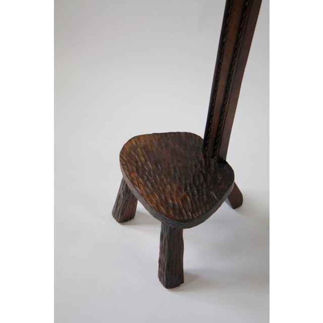 A sculptural three-legged side chair in stained and carved oak. The tall, narrow form draws attention to the texture of...
