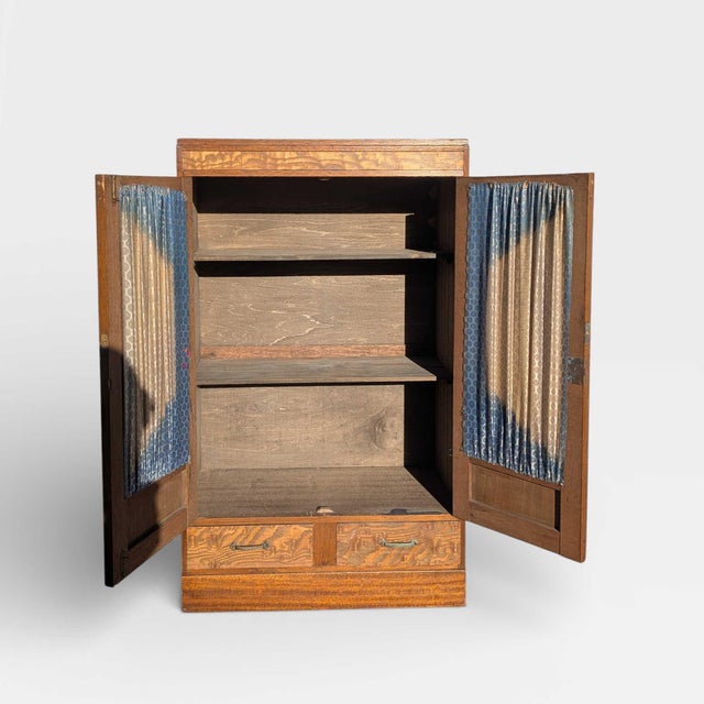 Early 20th century Japanese refinished wood cabinet with a compact vertical form, figured panel fronts, and fabric-backed...