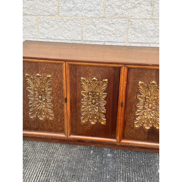 Mid-Century Modern 3-door server cabinet featuring ornate decorative front panels with raised floral motifs in gold-tone...