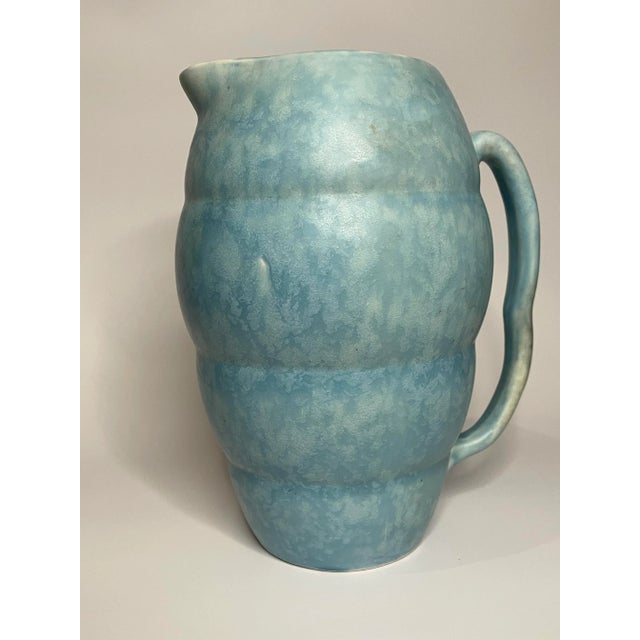 This ceramic 'made in England'' blue pitcher by Arthur Wood has a unique rippled design which lends to a modern,...
