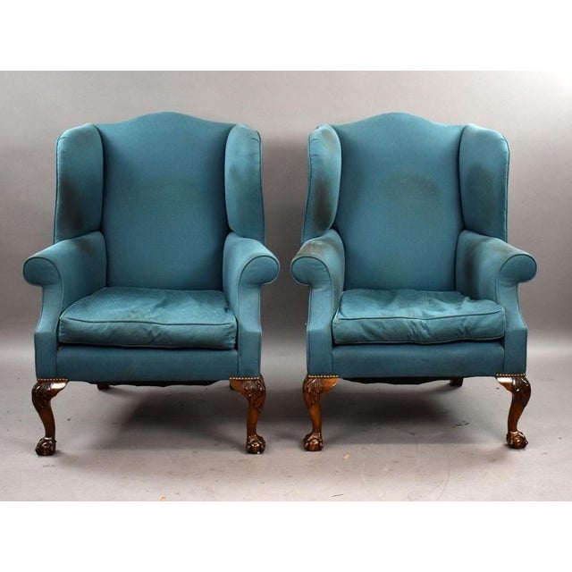 A smart pair of upholstered wingback armchairs, raised on carved cabriole legs with ball and claw feet. Each chair...