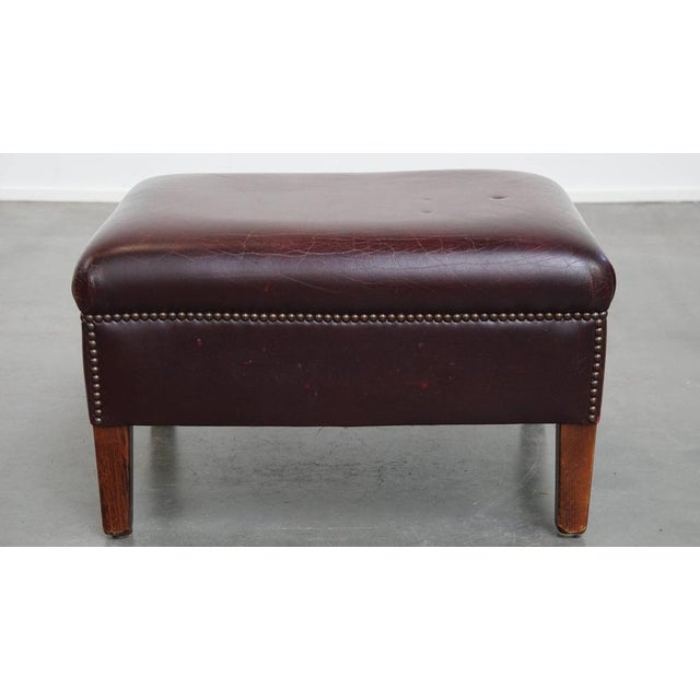 Offered this burgundy cowhide leather hocker/ footstool in English style. A cowhide leather footstool, also called hocker,...