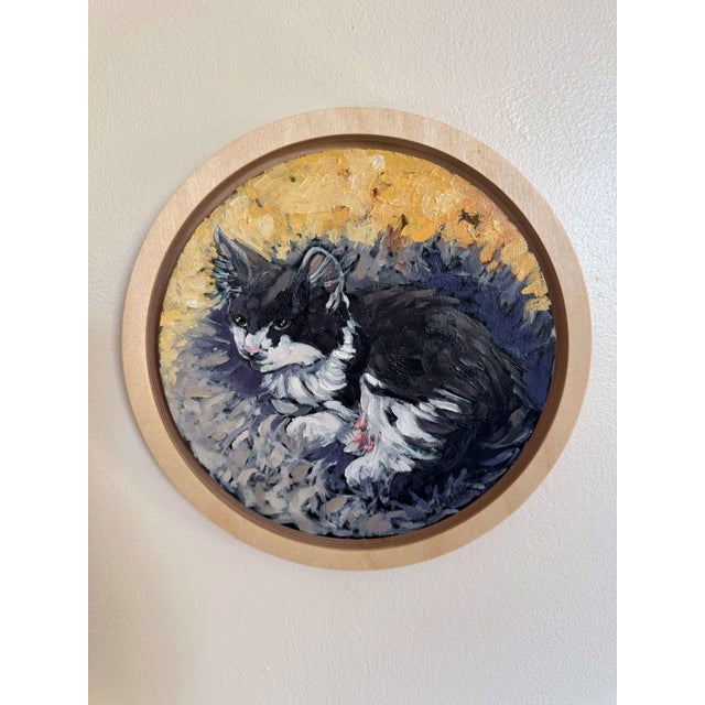 The artwork depicts a serene black and white cat nestled comfortably in a soft, textured setting, surrounded by warm...