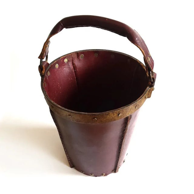 This is a mid-century fire bucket in reddish brown leather with metal rivets and a wood bottom.
