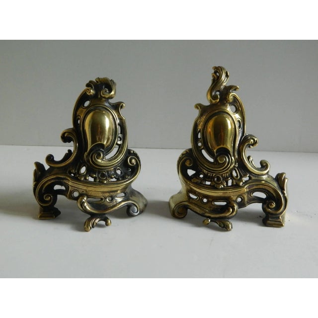 Pair of brass small chenets or andirons with shield and scrolls, 19th century.