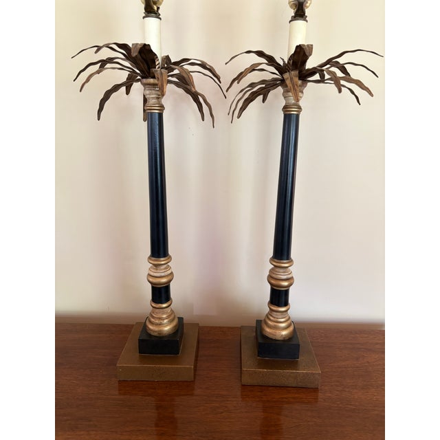 Pair of neoclassic candlestick lamps with stylized brass palm tree tops with a bud candleholder. Bodies are black and gold...