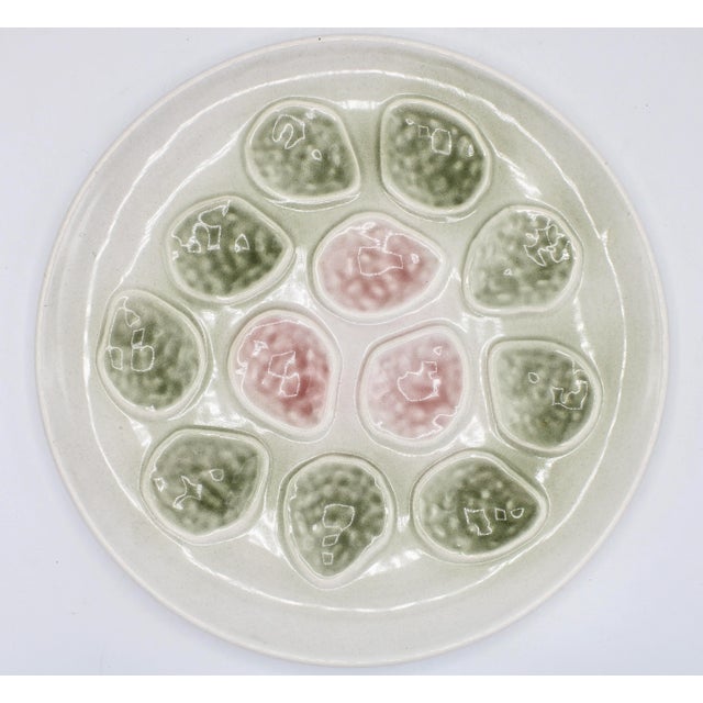A stunning French faïence ceramic oyster platter. 12 oyster wells in soft hues of seaweed green and pink against a creamy...