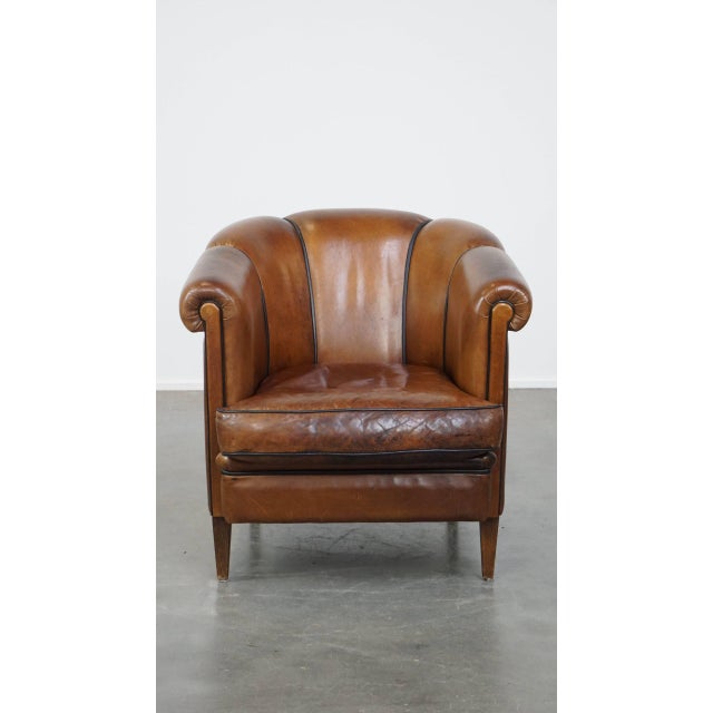 Unique vintage cognac-colored leather club chair with good seating comfort and a finish with black piping. This incredibly...