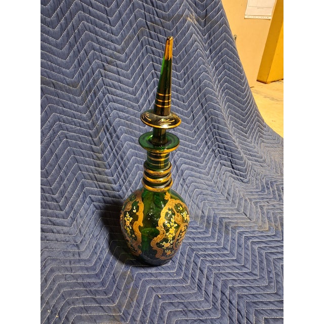 A striking antique Bohemian art glass decanter featuring a rich emerald green body embellished with hand-painted floral...