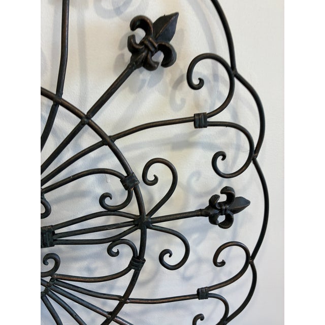 A substantial wrought metal wall sculpture featuring intricate scrollwork arranged in a circular, architectural form...